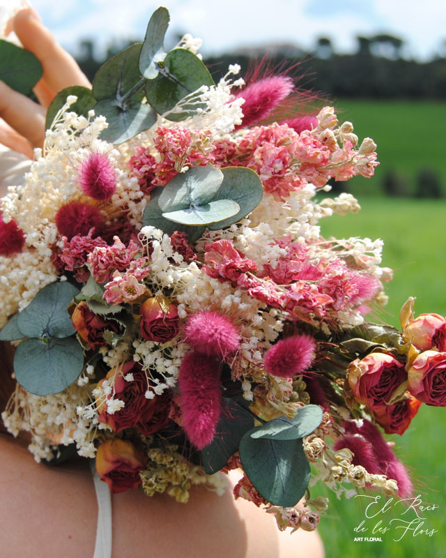 Mencía, ramo de novia en flor seca y preservada. De estilo desenfadado y forma pirámide. Compuesto por rosa roja seca, Bloom blanco, i relleno granate.