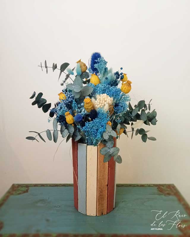 Jarrón de madera decorado con flores secas en tonos azul. Compuesto por: broom, eucalipto, papaver, phalaris. Medidas aprox.: 22 cm diámetro x 49 cm altura