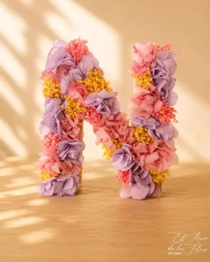 Letra con flor seca y preservada en tonos lila y rosa.