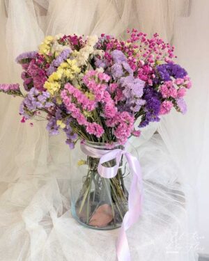 Ramo de statice seco mix de color, con paniculata fucsia seca. Jarrón de cristal con hojas de eucalipto en la base y lazada de raso lila. Medidas aprox: altura jarrón 20,50cm x 14cm diámetro en la base. Ramo diámetro 30cm x 40cm altura total